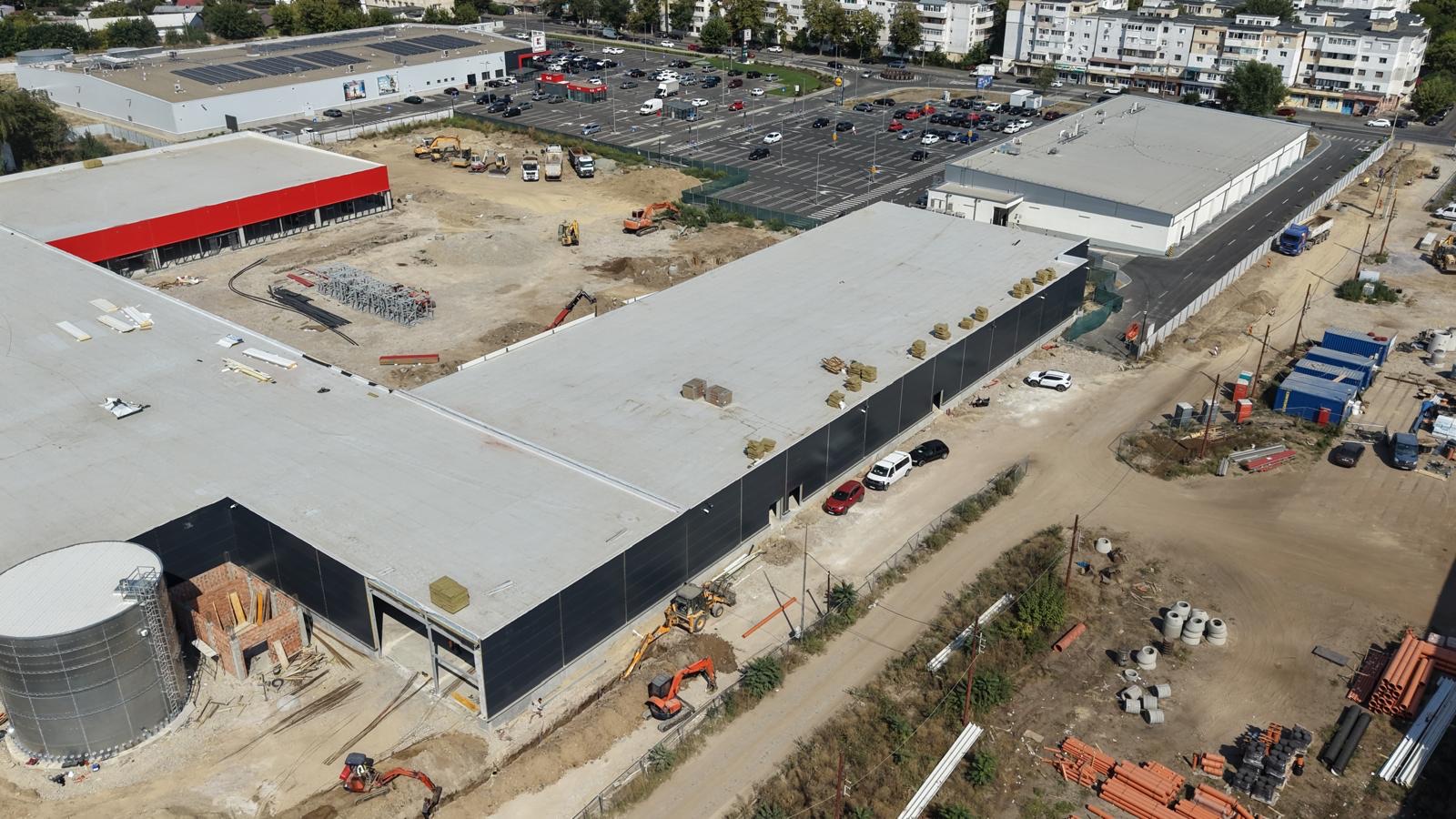 În perspectivă — rezervorul de incendiu în prim-plan, frontul parcului de retail în spate.